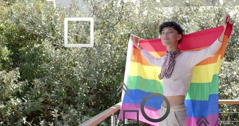Young man spreading rainbow pride flag on balcony, sunlit portrait expressing lgbtq pride