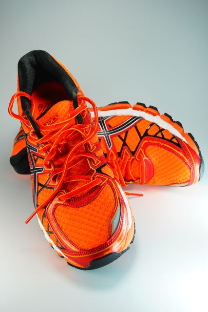 Bright orange athletic running shoes designed for sports activities, exhibiting synchronic details with rubber soles for enhanced traction. Suitable for promoting sportswear, fitness gear, and various workout and running accessories. Ideal for fitness campaigns, sports brands, or online stores specializing in active footwear.