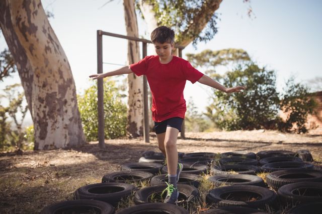 Young boy navigating through a tire obstacle course in a boot camp, balancing and focusing on his strides. Can be used for fitness and outdoor training activities, physical education, children's exercise programs, and teamwork challenges.