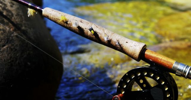 Close-up of a fishing rod with fly lures placed outdoors near a river. Ideal for illustrating outdoor recreational activities, fishing sports, angling equipment, and nature adventures. Perfect for promoting fishing products, fishing events, or outdoor gear.