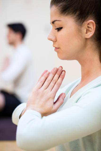 Woman sitting in lotus position with hands in prayer pose, focusing on meditation and mindfulness. Ideal for promoting yoga classes, wellness retreats, and mental health awareness campaigns.