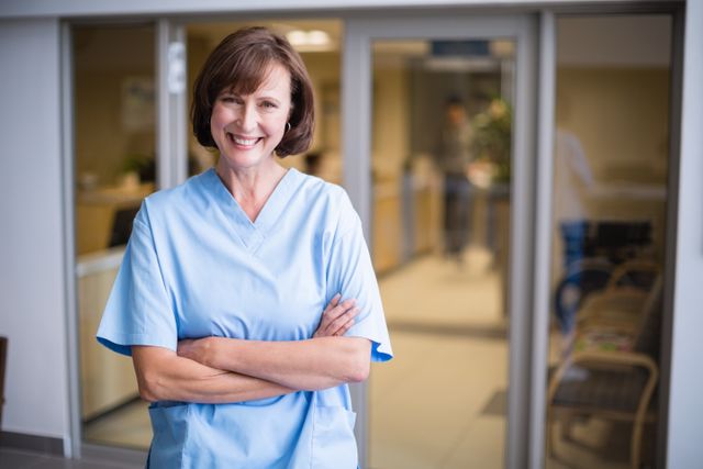 Portrait of smiling nurse standing with arms crossed in hospital corridor