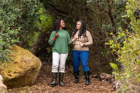African american women walking forest trail talking in sweaters and boots friendship