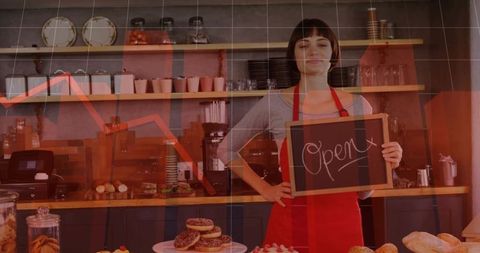 Young Barista Holding Open Sign While Serving Cozy Bakery Counter with Donuts and Bread