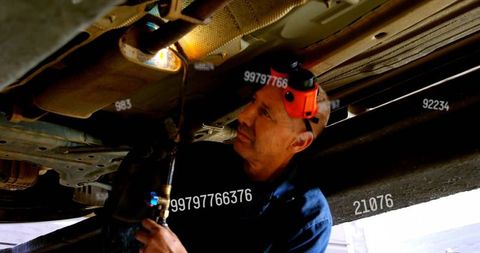 Mechanic inspecting vehicle undercarriage using headlamp during garage maintenance