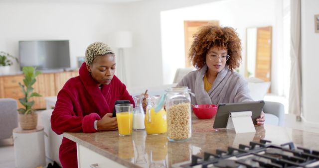 Two Women in Robes Having Breakfast and Using Gadgets in Modern Kitchen - Download Free Stock Images Pikwizard.com