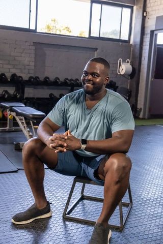 Smiling man sitting on plyometric box resting after workout in gym with smartwatch
