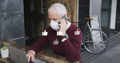 Businessman in Mask Using Smartphone and Laptop with Social Media Icons