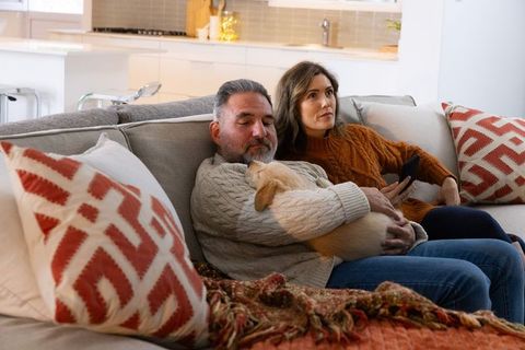 Middle-aged couple relaxing on sectional couch cuddling small puppy in cozy modern home