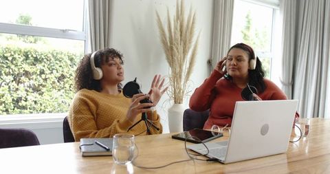Female podcasters recording conversation at home with laptop microphones headphones