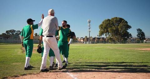 Multicultural Baseball Team Celebrating with Senior Coach at Home Plate on Sunny Field