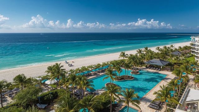 Turquoise oceanfront resort pool with palm islets, cabanas, sun loungers and sandy beach