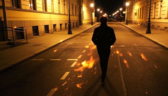 Silhouette walking alone on empty amber-lit city street at night with cinematic lamppost glow