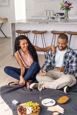 Couple enjoying indoor picnic with charcuterie board and wine on kitchen floor