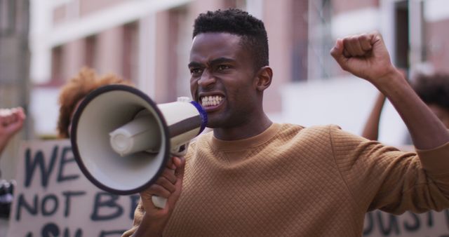 African american man shouting using megaphone with other people holding placards during protest. equal rights and justice protestors on demonstration march.
