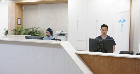 Multicultural clinic reception team working at modern desk wearing scrubs and hijab