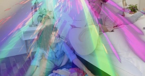 Two women sorting laundry on bedroom floor with straw hat and smartphone, colorful overlay