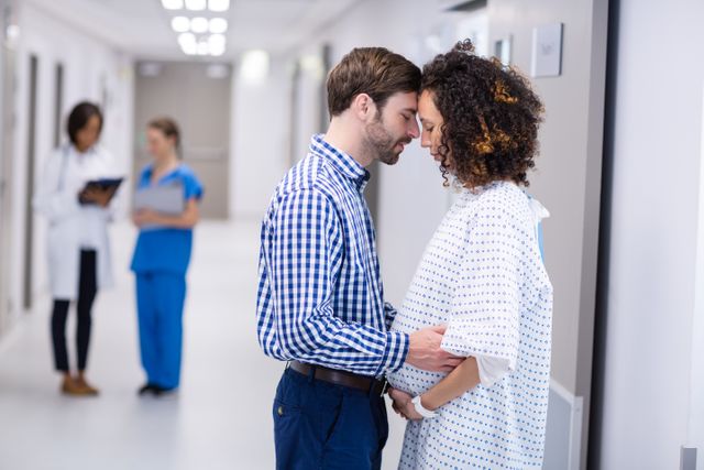 Man comforting pregnant woman in hospital corridor, showing support and care. Ideal for use in healthcare, maternity, and family-related content, emphasizing emotional support and relationships during pregnancy.
