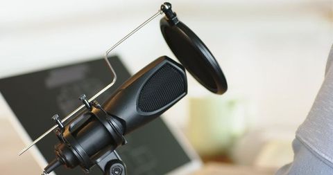 Black condenser podcast microphone on boom arm with pop filter in cozy home studio