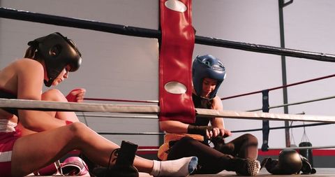 Female boxers sitting in corner tying gloves resting between rounds in boxing gym ring