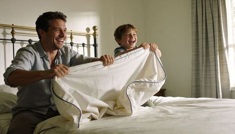 Father and son playing with duvet on bed laughing together cozy morning family bonding