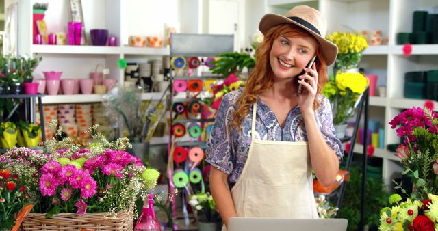 Female florist talks on phone while surrounded by vibrant flowers. Ideal for advertising, small business promotions, floral industry content, customer service concepts, and entrepreneurship features.