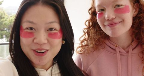 Smiling diverse friends wearing pink under-eye patches, posing for skincare routine