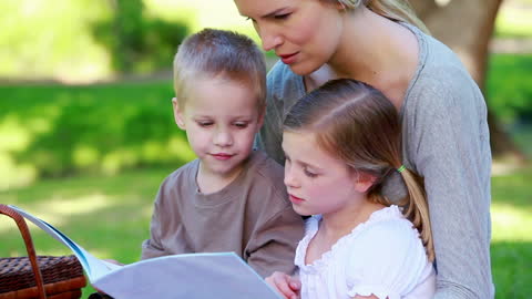Mother Reading Picture Book with Children in Park