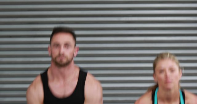 Blurry image of a man and a woman engaged in an exercise routine in front of a metal wall. This image captures the dynamic movement of a fitness activity. It could be used in blog posts, articles, or advertisements related to fitness, active lifestyle, or health products.