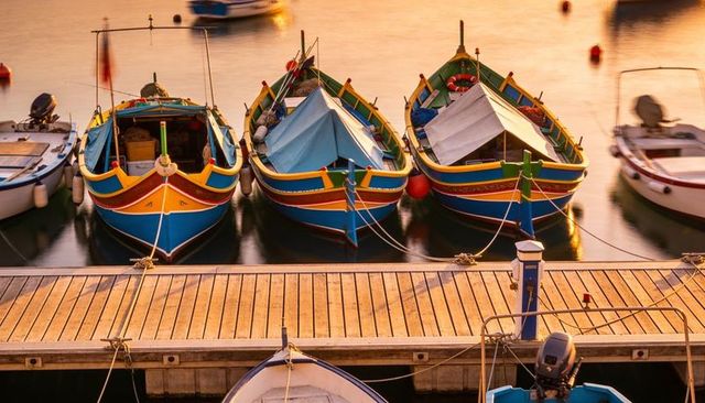 Colorful wooden fishing boats bobbing at sunlit marina dock with reflections