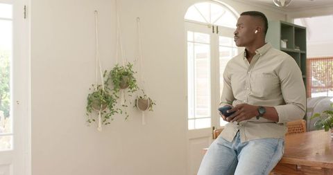 African american man sitting on wooden table using smartphone wearing earbuds and watch