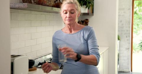 Senior Woman Stirring Drink in Stylish Modern Kitchen