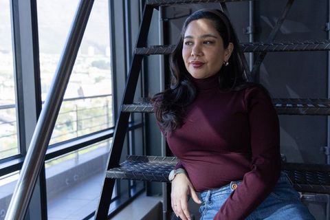 Thoughtful professional woman sitting on metal stairs by large office windows wearing wristwatch