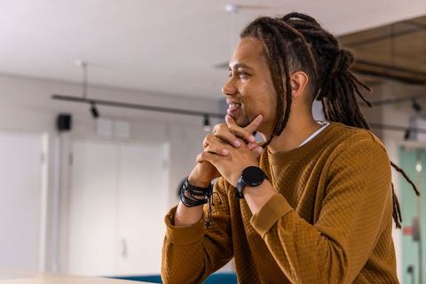 African American man leaning on desk in modern coworking space, thinking and smiling confidently