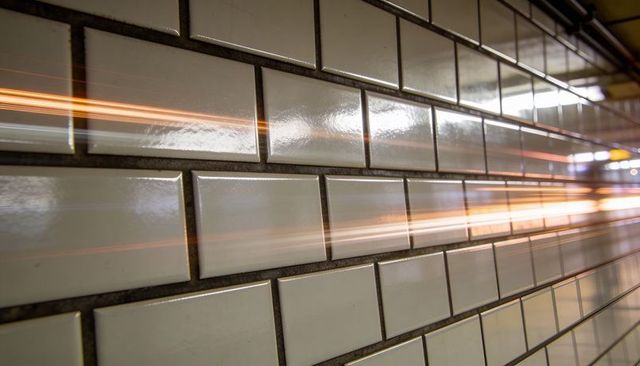 Glossy ceramic subway tile wall receding into underground corridor with orange light trails