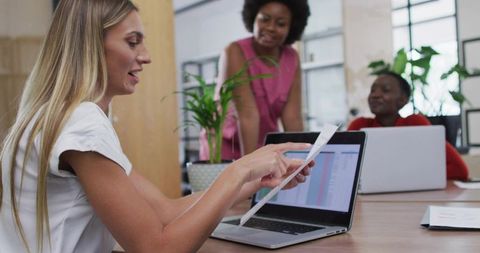 Woman Leading Team Meeting Pointing at Spreadsheet on Laptop with Printed Report