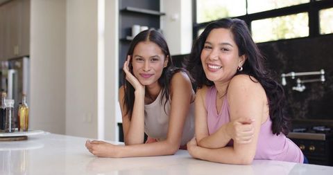 Two friends leaning on kitchen countertop smiling, casual home lifestyle portrait
