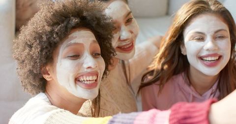 Diverse friends enjoying facial masks taking selfie during cozy home spa moment