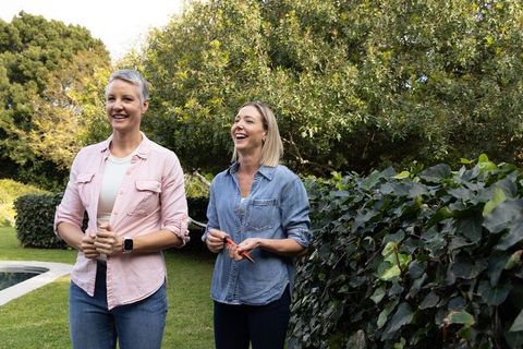 Two women gardening pruning lush ivy hedge poolside, laughing and enjoying outside