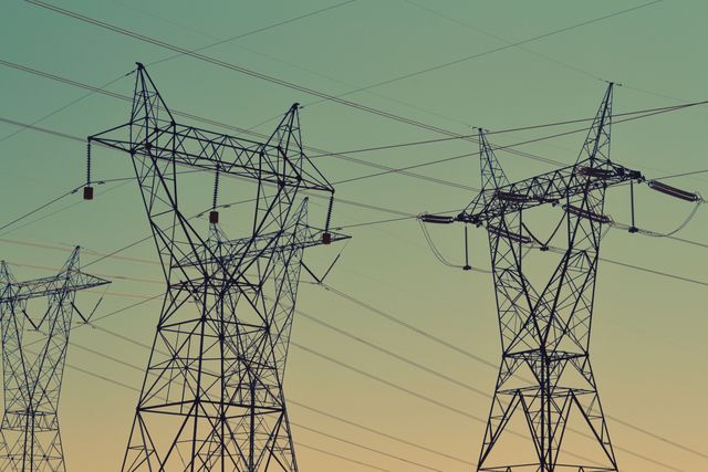 Silhouette of high voltage power lines and electrical towers against a clear sky at sunset, highlighting the infrastructure and energy networks. Ideal for use in articles related to energy production, electricity supply, industrial engineering, and utility grid systems.