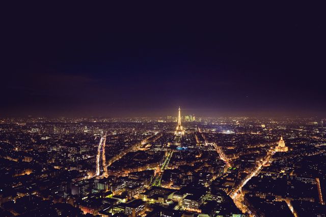 A stunning aerial night view of Paris with the Eiffel Tower prominently lit up, surrounded by the glowing city lights. Perfect for travel blogs, tourism brochures, and posters promoting Parisian landmarks and nightlife.