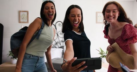 Joyful Friends Packing and Taking Selfie in Holiday Bedroom