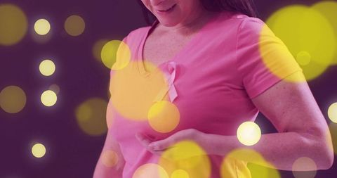 Mid-adult woman wearing pink breast cancer ribbon adjusting tee amid warm bokeh lights