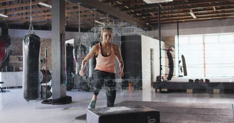 Female athlete performing plyometric box jump in industrial gym, training and conditioning