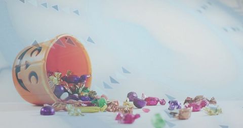 Orange jack-o'-lantern bucket spilling colorful foil candies on pale tabletop