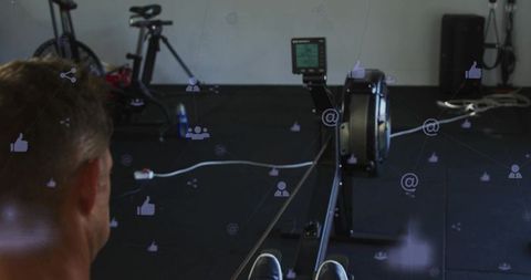 Fit man rowing on indoor erg machine in gym with fitness monitor, bikes and training mats