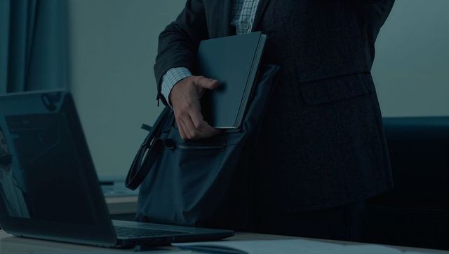 Businessman Sliding Slim Tablet into Leather Bag Next to Open Laptop for Commuter Workflow