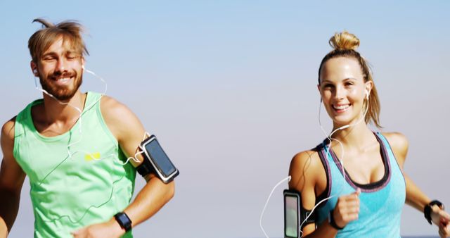 A young Caucasian man and woman are jogging together, wearing sportswear and listening to music, with copy space. Their active lifestyle and enjoyment of fitness are evident as they share a moment of exercise under a clear sky.