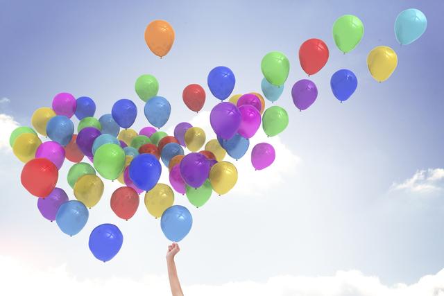 Digital composite of hand reaching to colourful balloons 