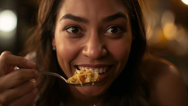 Smiling young woman enjoying cheesy bite with spoon in warm bokeh restaurant portrait